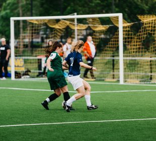 women playing soccer on green field during daytime